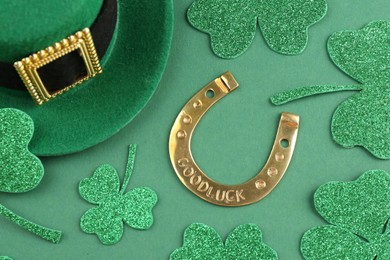 St. Patrick's day. Leprechaun hat, golden horseshoe and decorative clover leaves on green background, above view
