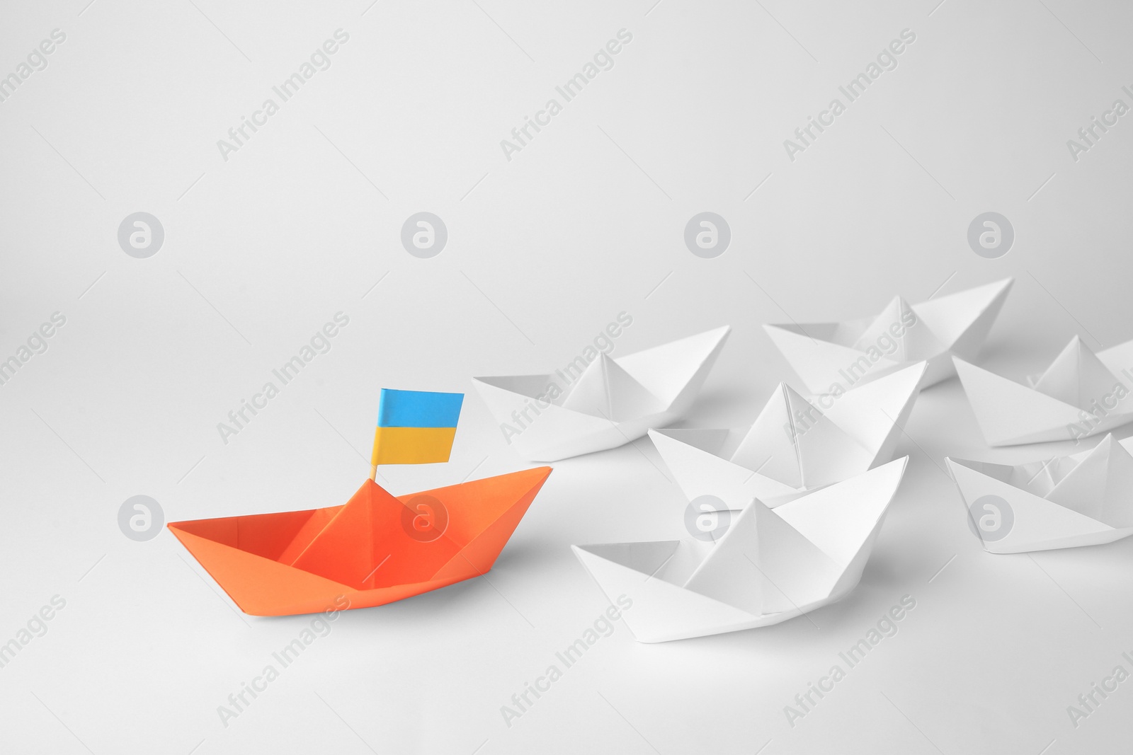 Photo of Group of paper boats following orange one on white background. Leadership concept