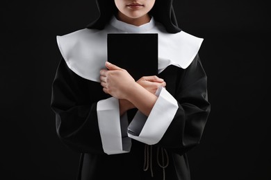 Nun with Bible on black background, closeup