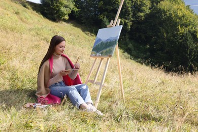Photo of Young woman drawing on easel with brush near forest