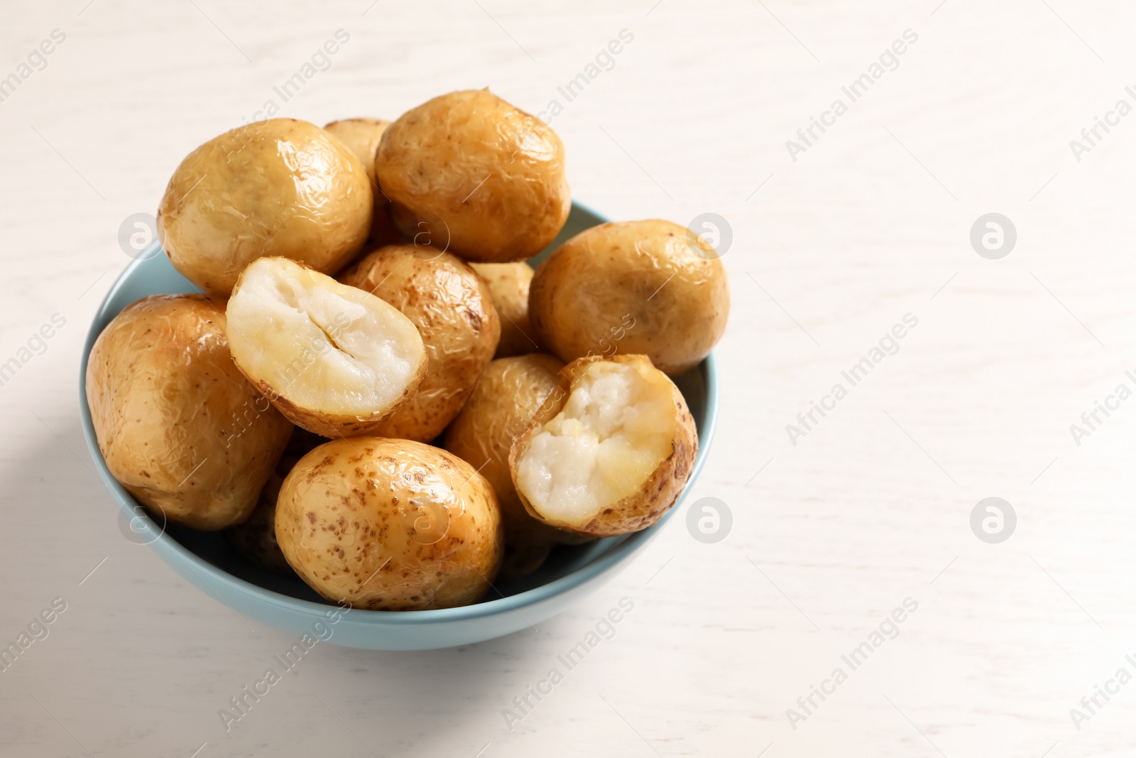 Photo of Bowl of tasty whole baked potatoes on white table, space for text