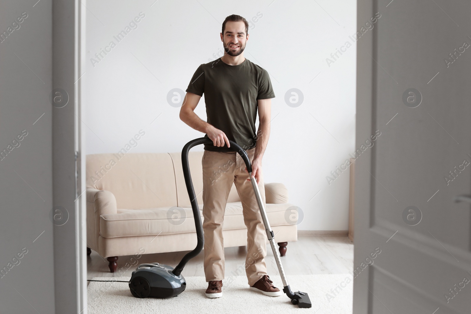 Photo of Young man cleaning carpet with vacuum in living room