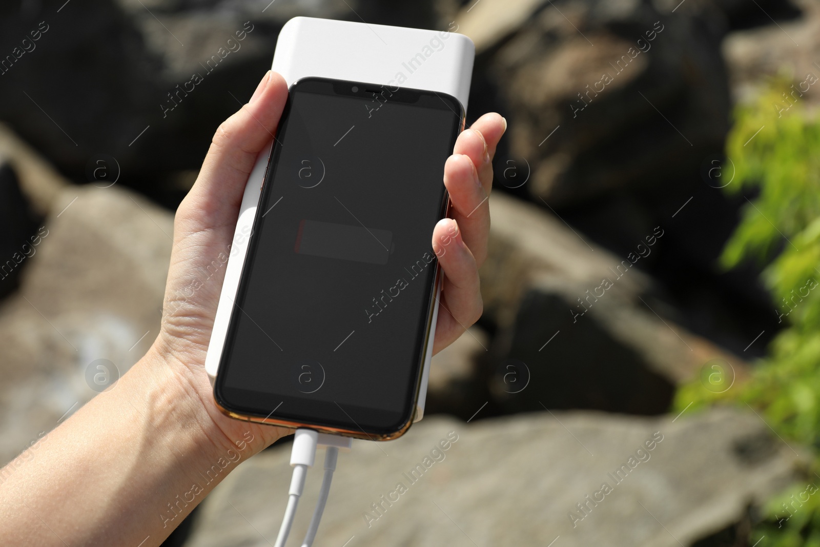 Photo of Woman charging smartphone with power bank on rocky mountain, closeup