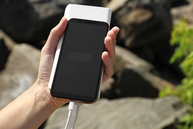 Woman charging smartphone with power bank on rocky mountain, closeup