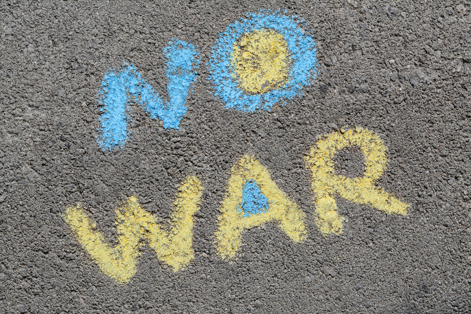 Photo of Words No War written with blue and yellow chalks on asphalt outdoors, top view