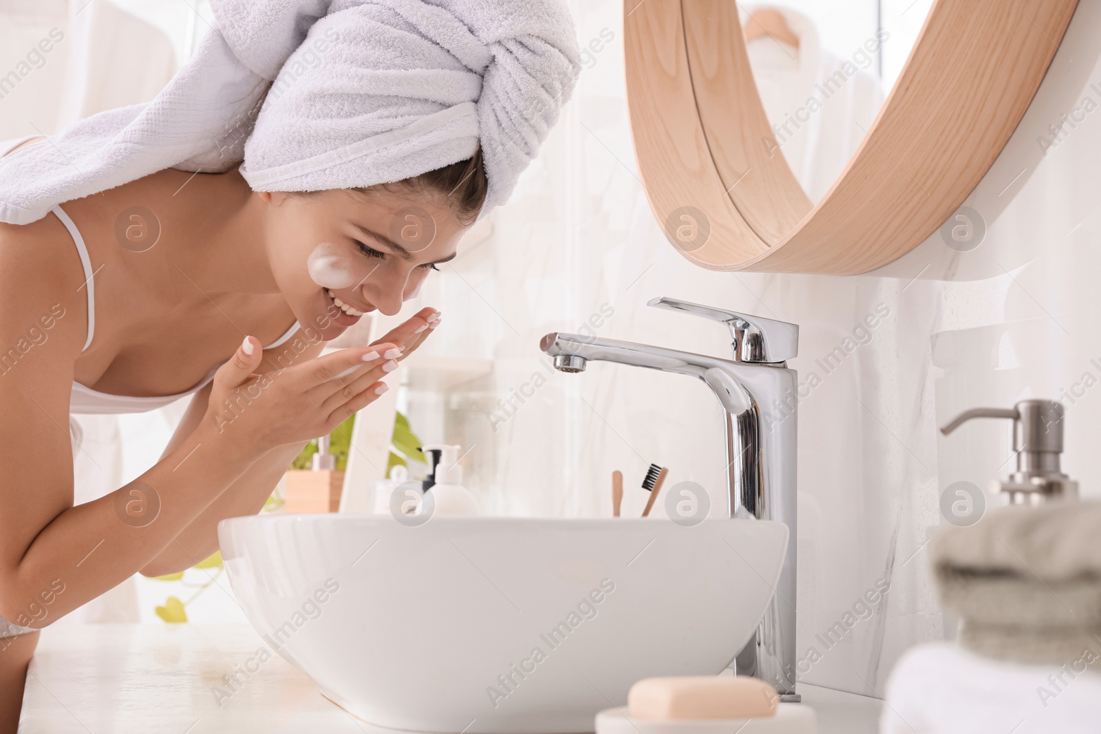 Photo of Beautiful teenage girl washing face with cleansing foam in bathroom. Skin care cosmetic