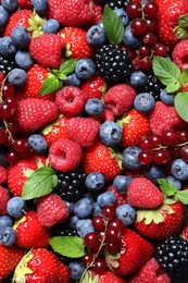 Photo of Assortment of fresh ripe berries with green leaves as background, top view