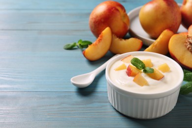 Photo of Delicious yogurt with fresh peach and mint on light blue wooden table, space for text