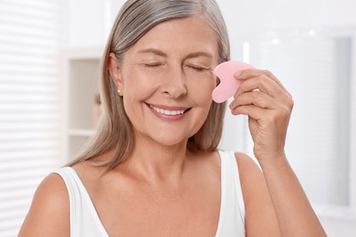 Woman massaging her face with rose quartz gua sha tool in bathroom