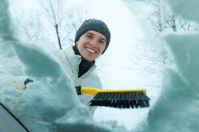 Photo of Man cleaning snow from car windshield, view from inside
