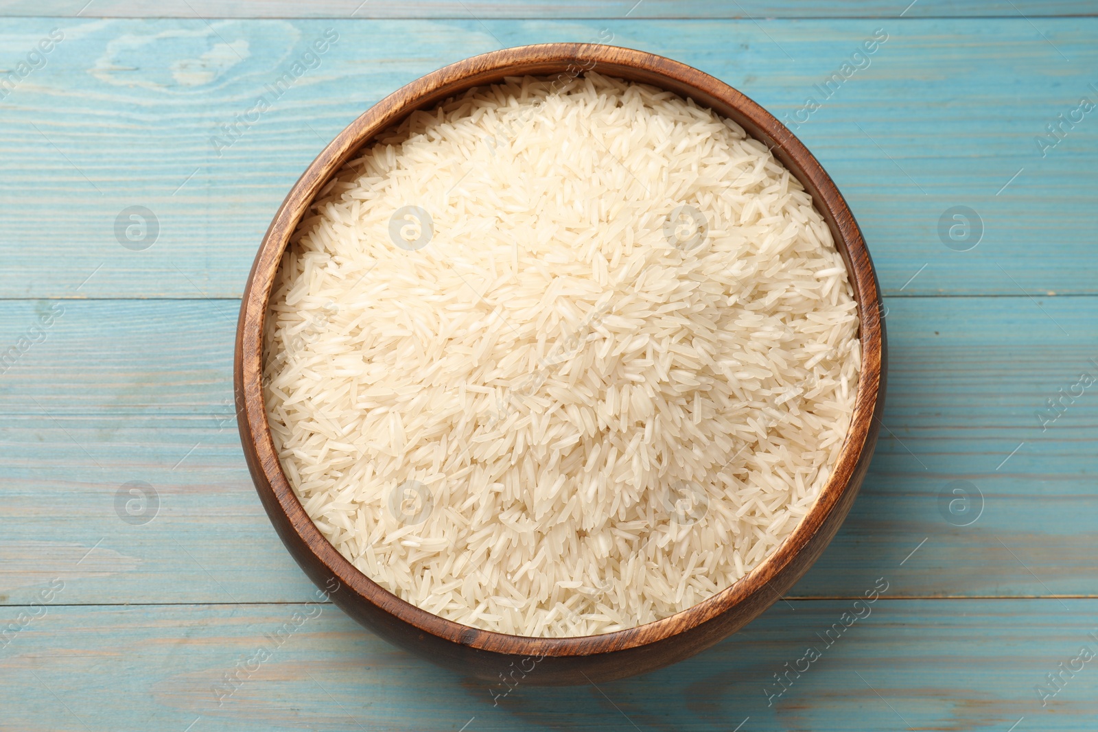 Photo of Raw basmati rice in bowl on light blue wooden table, top view