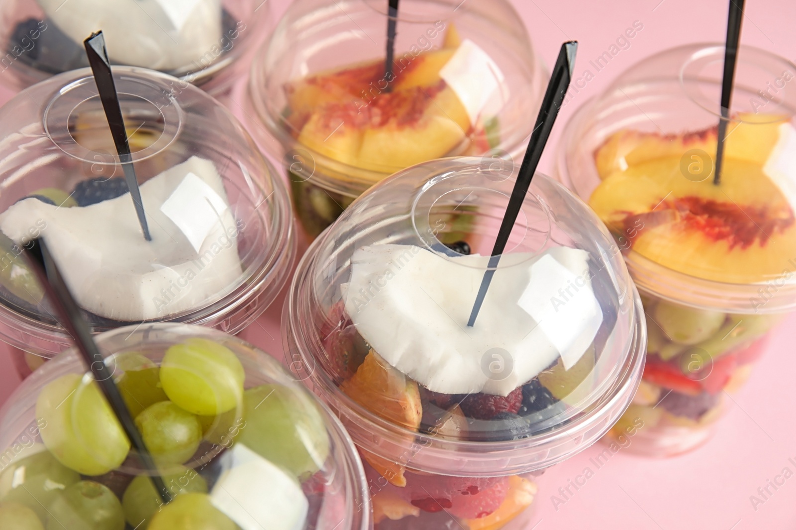 Photo of Fresh tasty fruit salad in plastic cups on pink table, closeup