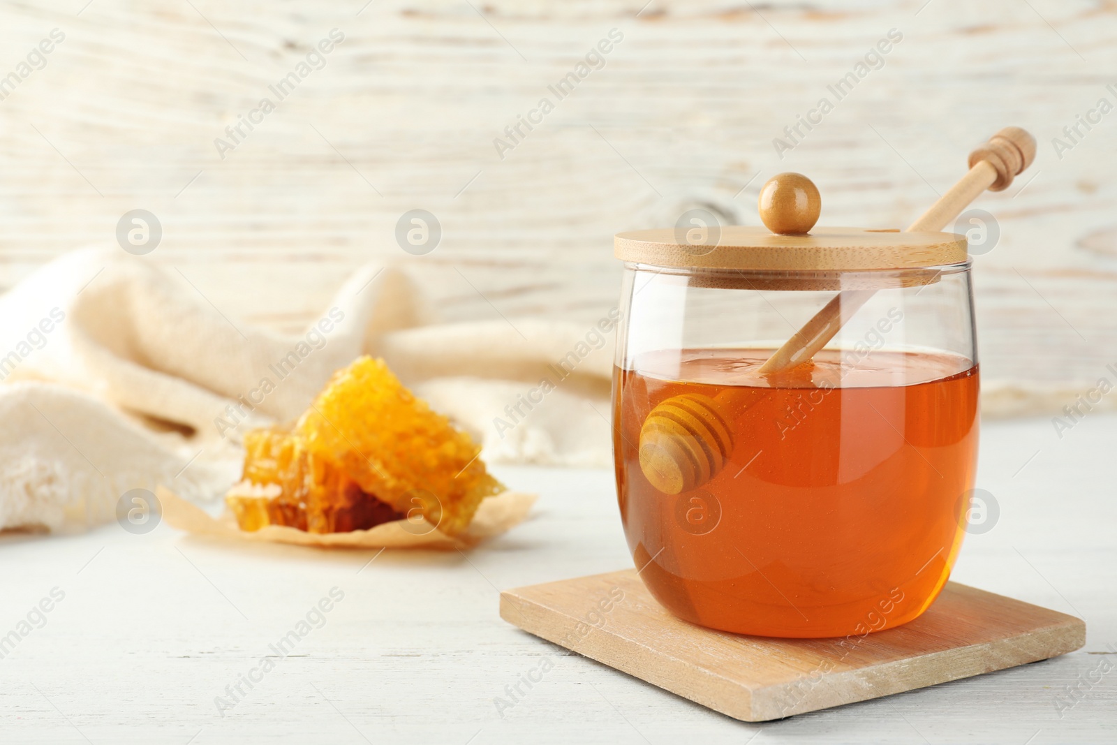 Photo of Glass jar with sweet honey and dipper on table. Space for text