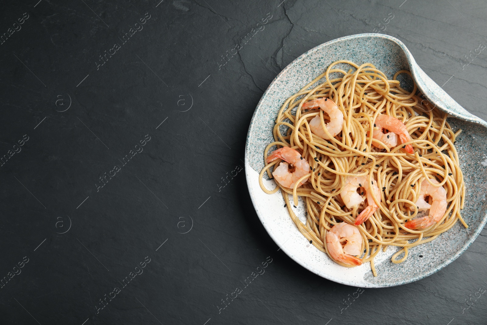 Photo of Plate of tasty buckwheat noodles with shrimps on black table, top view. Space for text