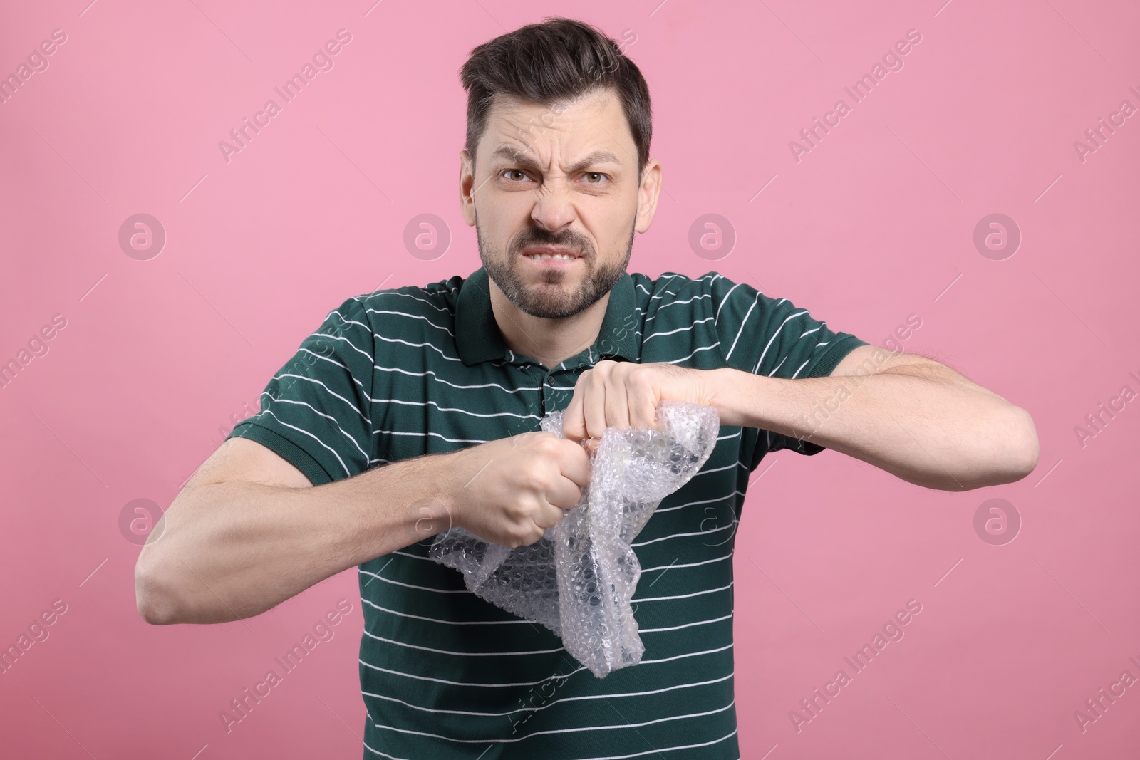 Photo of Angry man popping bubble wrap on pink background. Stress relief