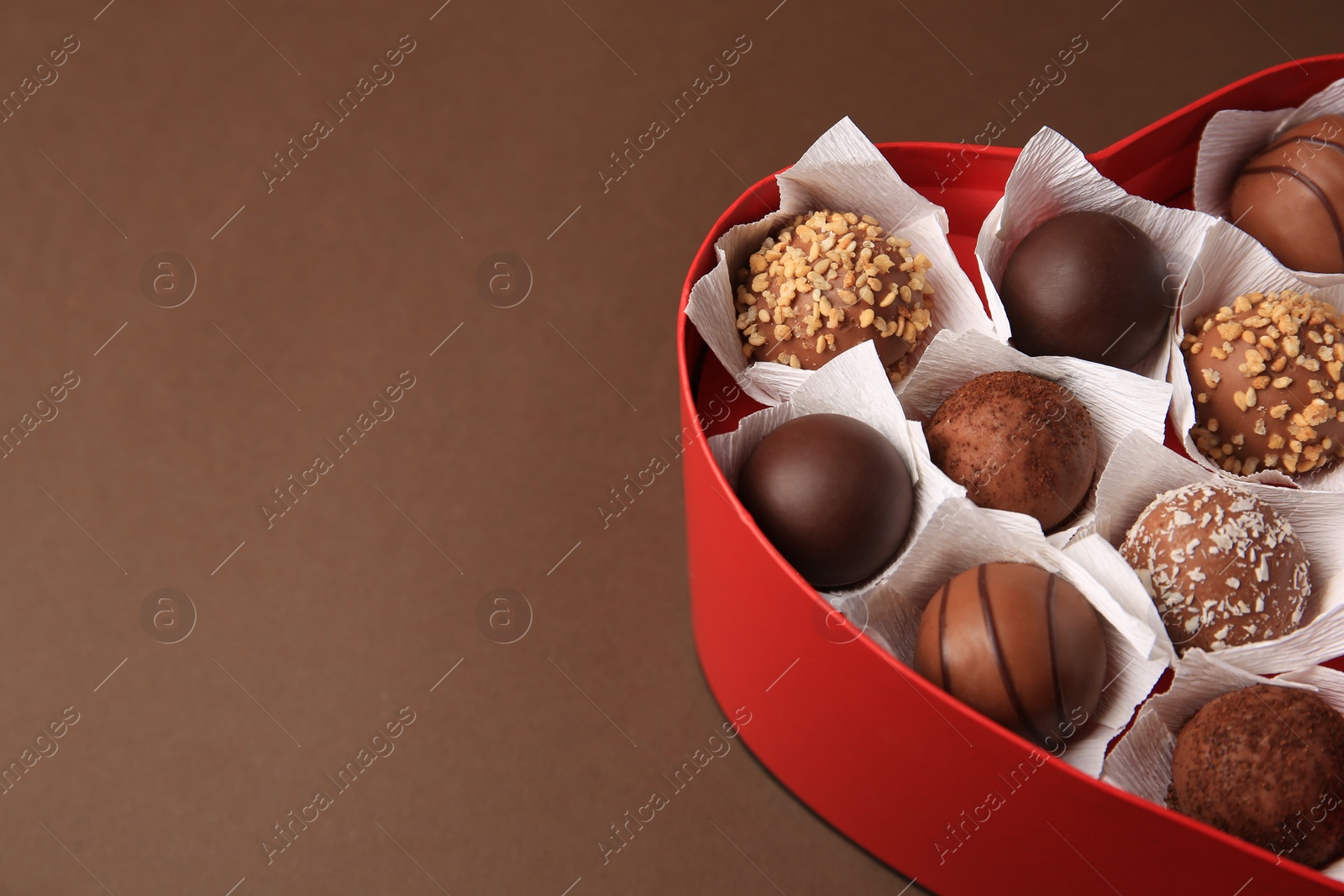 Photo of Heart shaped box with delicious chocolate candies on brown background, closeup. Space for text