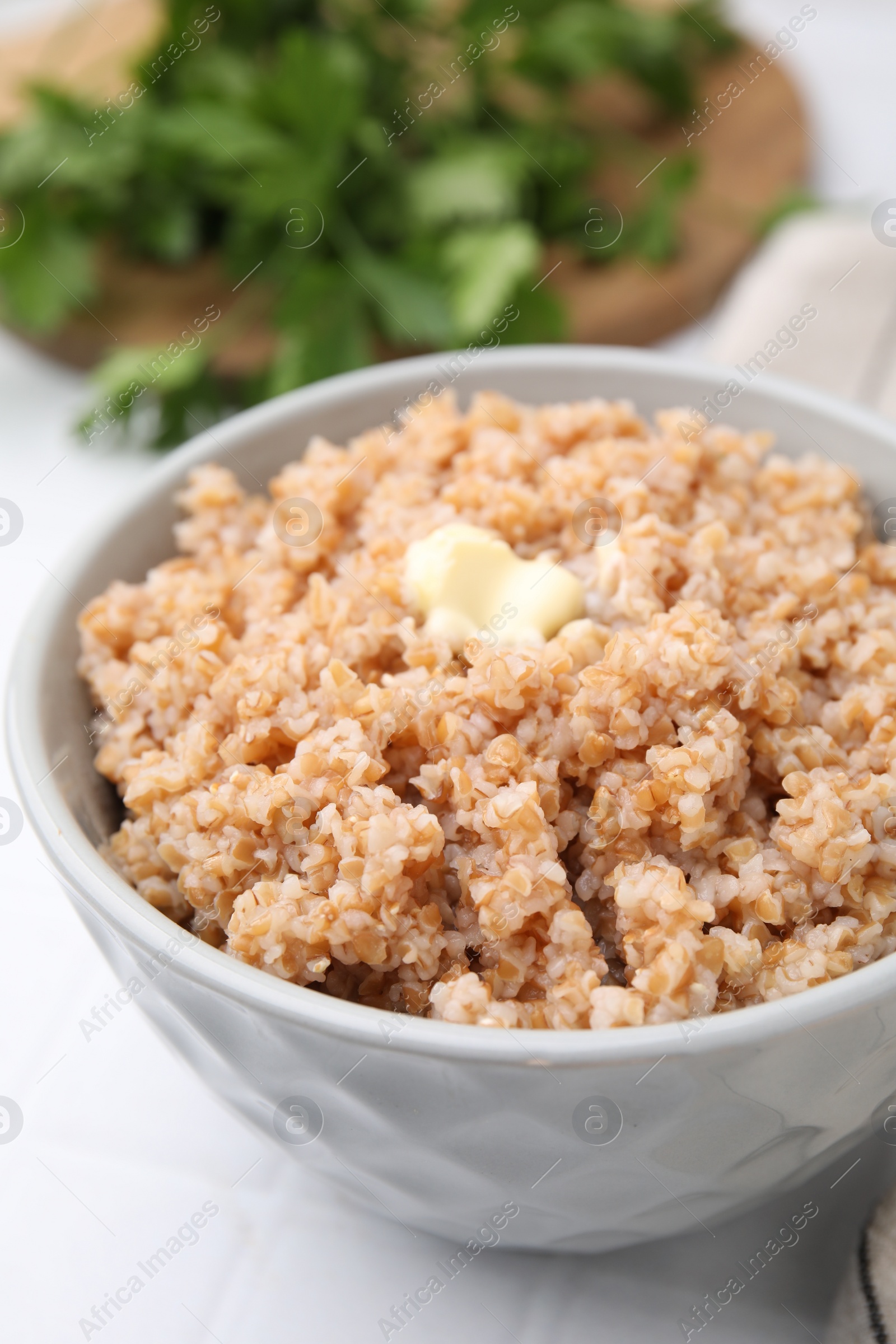 Photo of Tasty wheat porridge with butter in bowl on white table, closeup