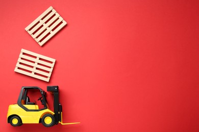 Photo of Toy forklift and wooden pallets on red background, flat lay. Space for text