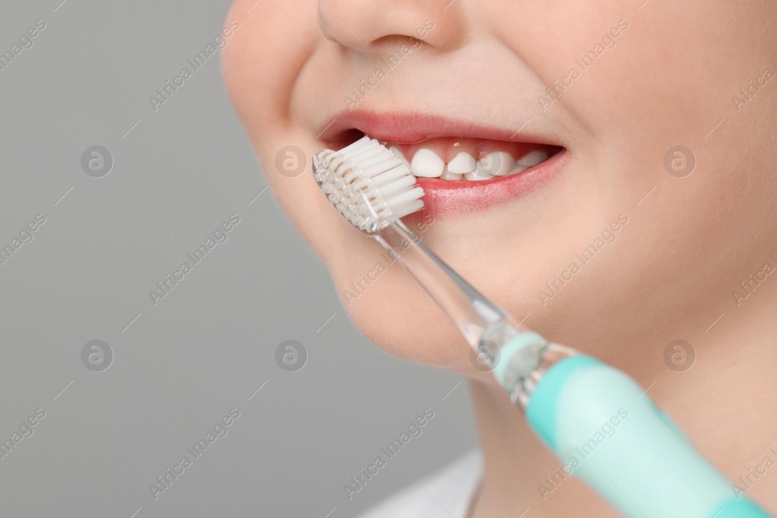 Photo of Cute little boy brushing his teeth with electric toothbrush on light grey background, closeup. Space for text