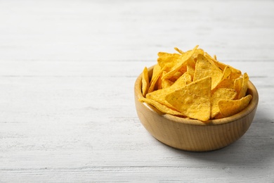 Tasty mexican nachos chips in bowl on white wooden table. Space for text