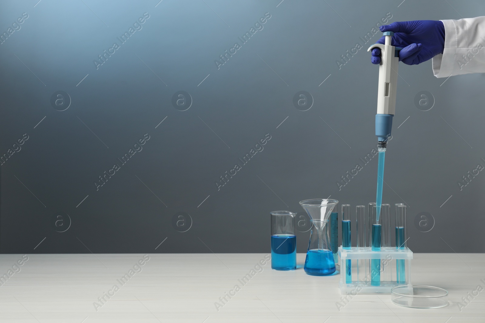 Photo of Laboratory analysis. Scientist dripping sample with micropipette into test tube at white wooden table, closeup. Space for text