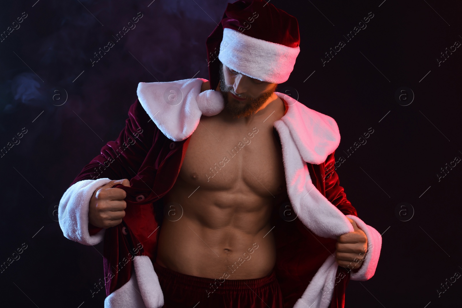 Photo of Attractive young man with muscular body in Santa costume on black background