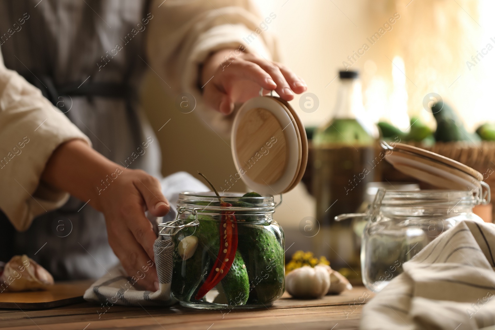 Photo of Woman pickling glass jar of cucumbers at wooden table, closeup