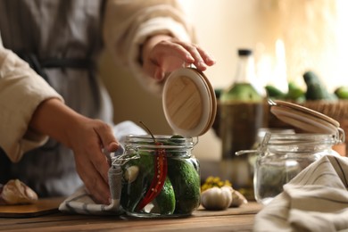 Woman pickling glass jar of cucumbers at wooden table, closeup