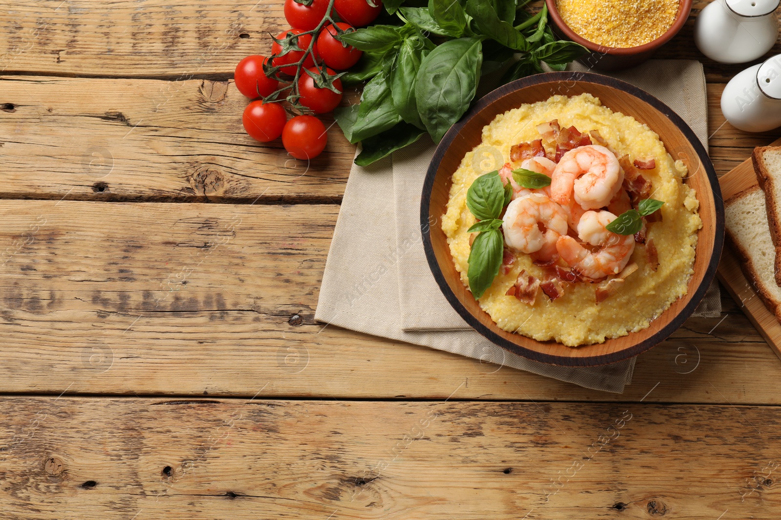Photo of Fresh tasty shrimps, bacon, grits and basil in bowl on wooden table, flat lay. Space for text