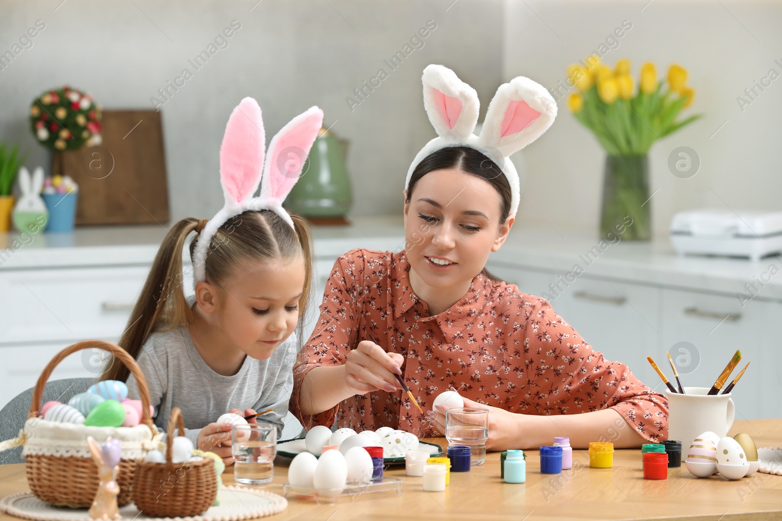 Photo of Mother and her cute daughter painting Easter eggs at table in kitchen