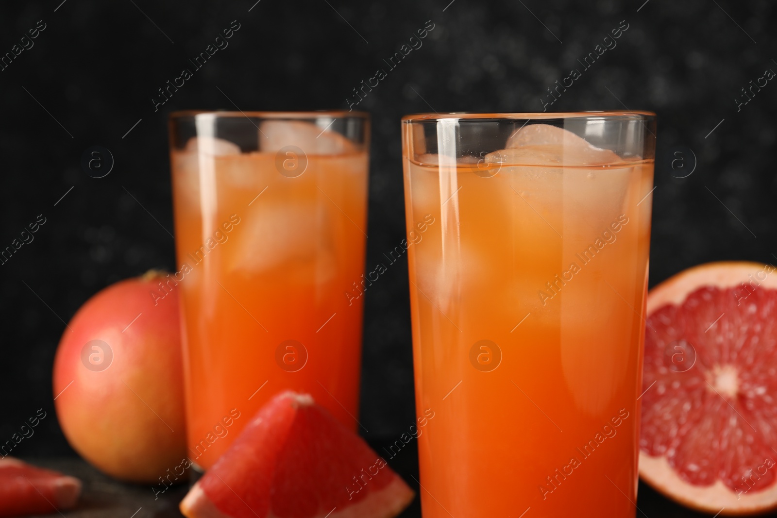 Photo of Tasty grapefruit drink with ice in glasses and fresh fruits on table, closeup