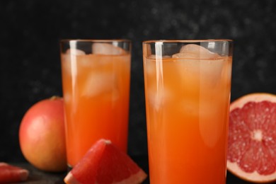 Photo of Tasty grapefruit drink with ice in glasses and fresh fruits on table, closeup