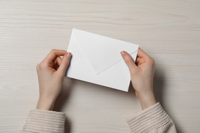 Photo of Woman with letter envelope at light wooden table, top view