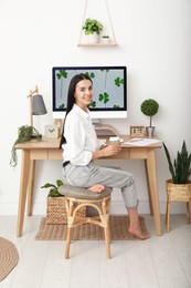 Photo of Young woman with cup of drink at table in room. Home office