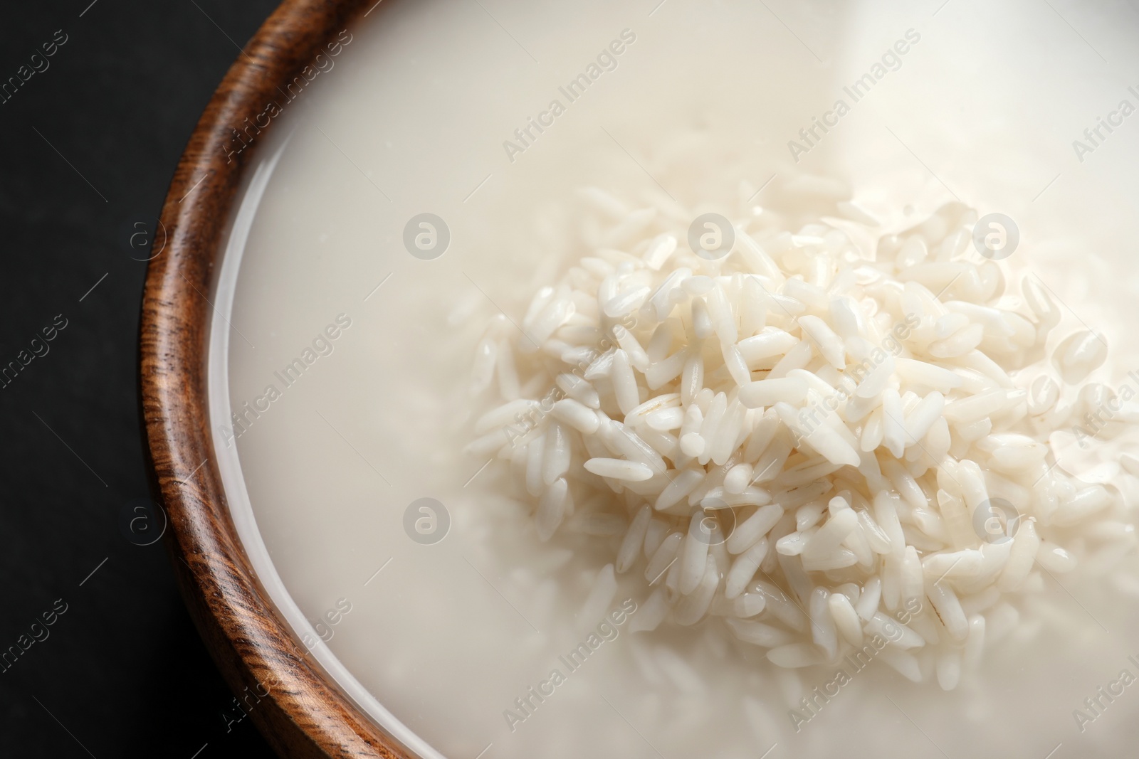 Photo of Rice soaked in water on black table, closeup