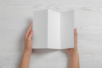 Photo of Woman with blank brochure on wooden background, above view. Mock up for design