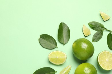 Photo of Whole and cut fresh ripe limes with leaves on light green background, flat lay