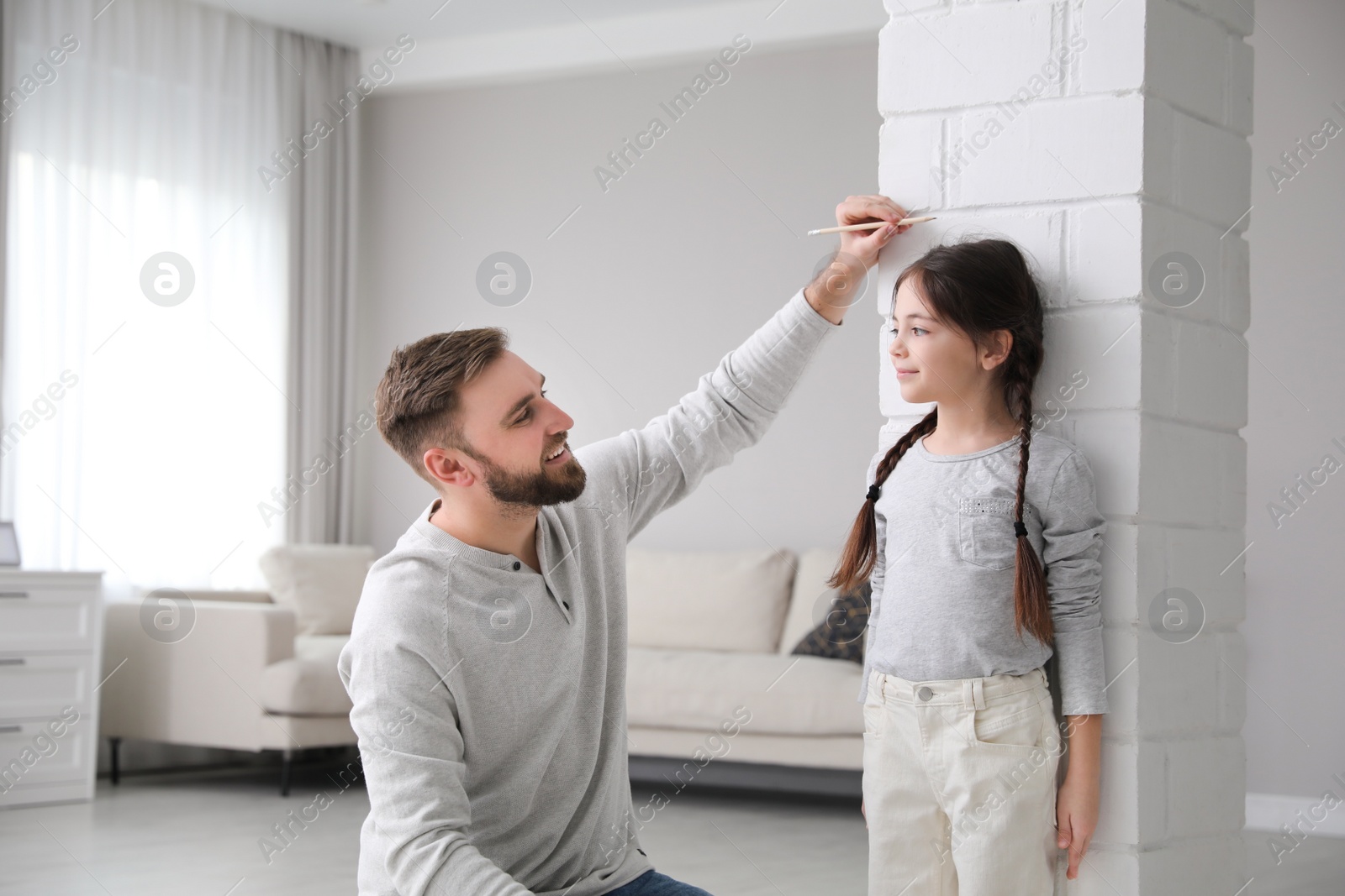 Photo of Father measuring daughter's height near white brick pillar at home