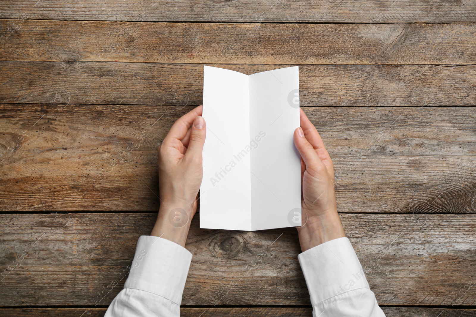 Photo of Young woman holding blank brochure at wooden table, top view. Mock up for design