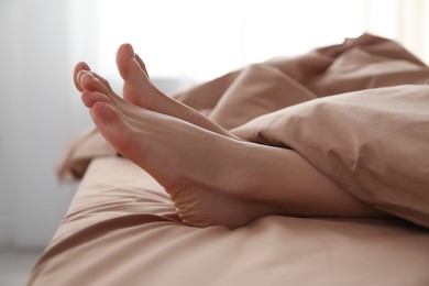 Photo of Person in bed with brown linens at home, closeup on feet