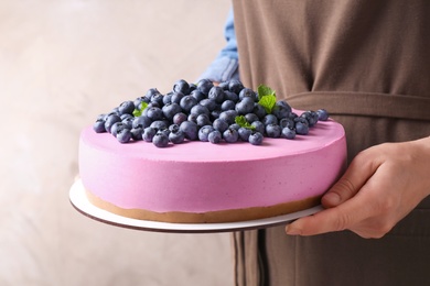 Photo of Young woman holding tasty blueberry cake on beige background, closeup