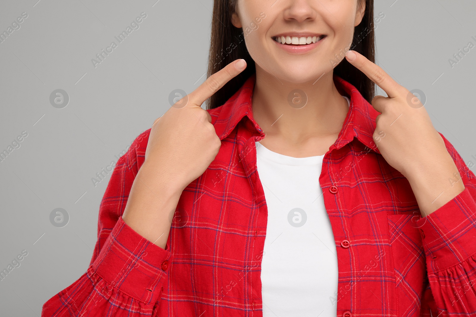 Photo of Woman pointing at her clean teeth and smiling on light grey background, closeup