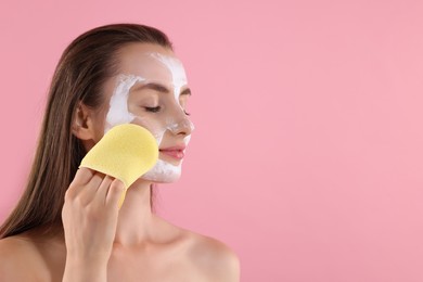 Photo of Happy young woman washing off face mask with sponge on pink background. Space for text