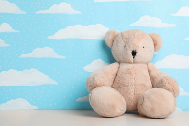 Teddy bear on white table near wall with painted blue sky, space for text. Baby room interior