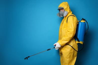 Photo of Man wearing protective suit with insecticide sprayer on blue background, space for text. Pest control