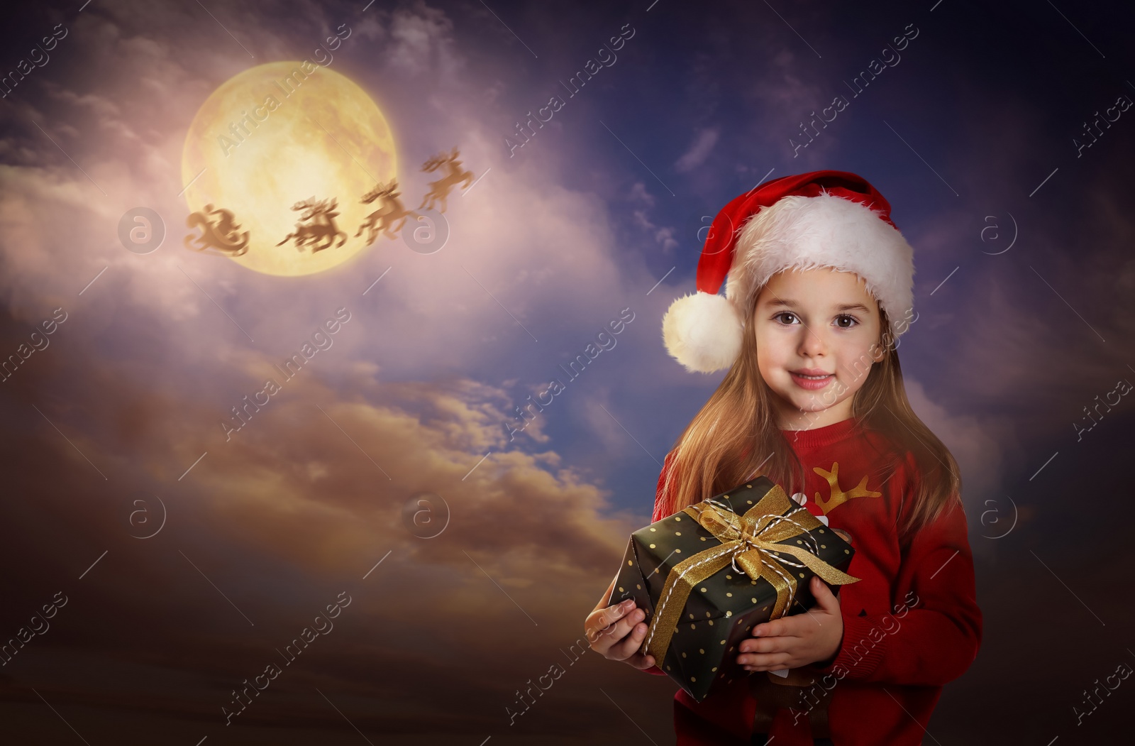 Image of Cute child with Christmas gift and Santa Claus flying in his sleigh on background