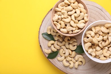 Tasty cashew nuts and green leaves on yellow background, top view. Space for text