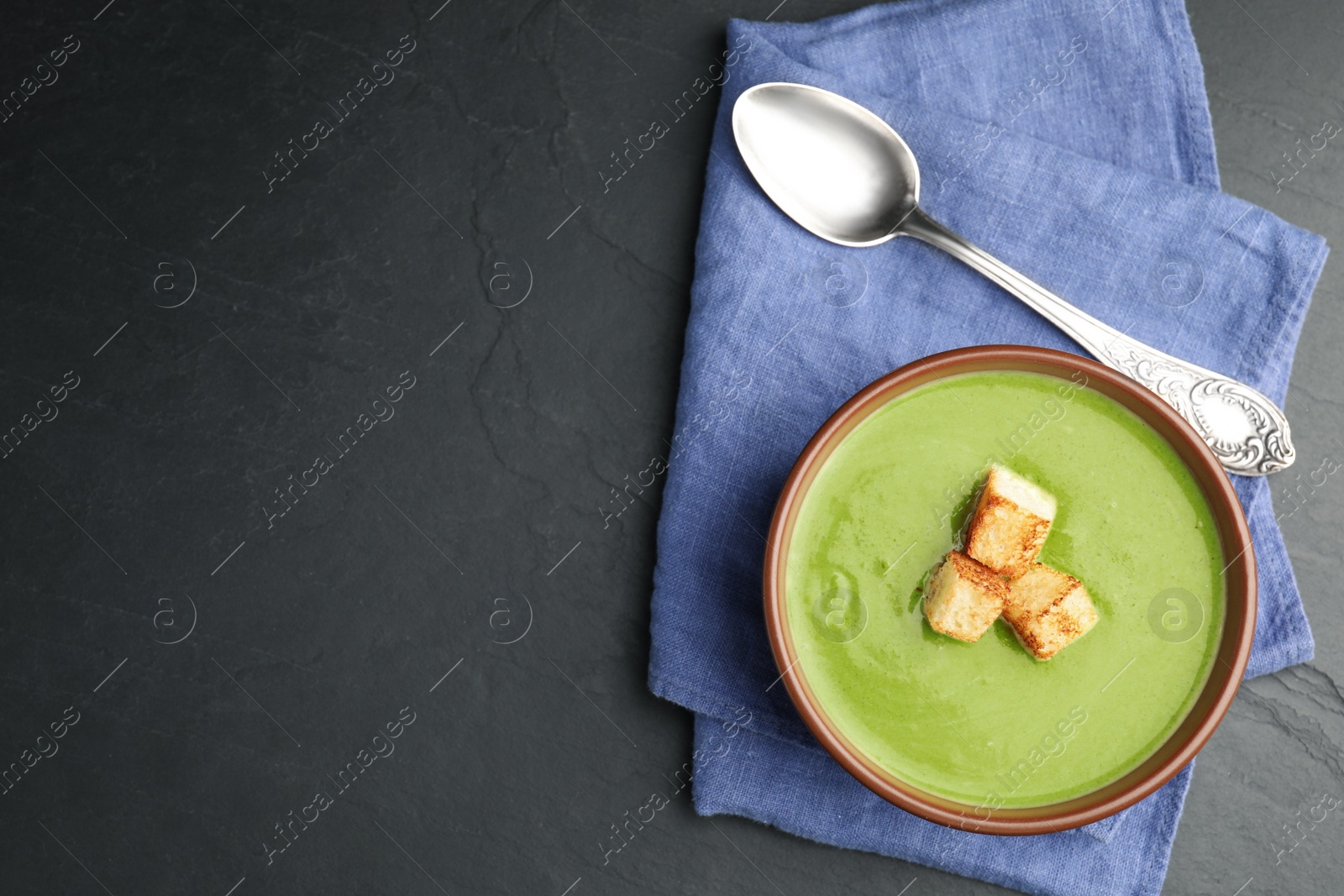 Photo of Delicious broccoli cream soup served on dark grey table, top view. Space for text