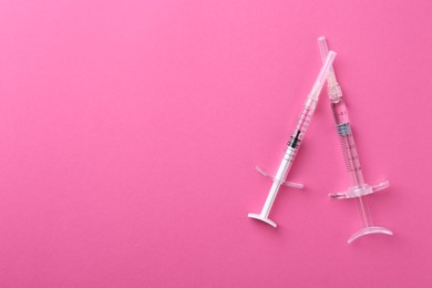 Photo of Injection cosmetology. Two medical syringes on pink background, top view. Space for text