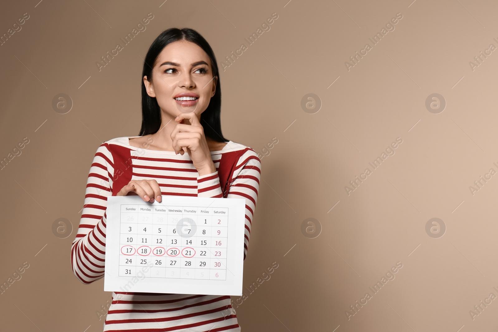 Photo of Pensive young woman holding calendar with marked menstrual cycle days on beige background. Space for text